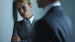 © A2Z AI  - Serious young business woman with blonde hair in professional suit listens attentively to blurred male colleague in a modern corporate setting