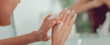 © Prostock-studio - A person uses their fingers to apply cream to their hands while looking in a mirror. The setting is a bathroom with natural light coming in.