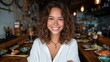 © svastix - A cheerful woman with curly hair beams at the camera while seated in a trendy restaurant, showcasing her joy and the vibrant atmosphere around her filled with delicious food.