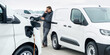 © scharfsinn86 - Fleet manager with digital tablet and smartphone supervising rows of white electric delivery vans