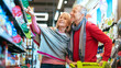 © Prostock-studio - A senior couple is shopping in a grocery store. They are smiling and looking at items on the shelves. The man points at a product while the woman looks at him, both enjoying their time together.