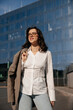 © verona_studio - Pretty Woman Wearing White Shirt And Glasses Holding Blazer Near Modern Office Building. Casual Business Lifestyle Concept Female Urban Style