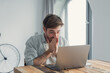 © Daniel - Young man reacting to surprising news or unexpected information on his laptop, expressing disbelief and wonder while sitting at a wooden desk in a bright room