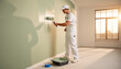© Alex & M Studio - Professional male painter in white overalls using roller to paint interior wall light green during home renovation project in bright empty room interior design and house redecorating service concept