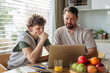© Halfpoint - Father helping teenage son with diabetes with homework on laptop in kitchen.