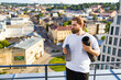 © sofiko14 - A man with a beard and long hair tied back stands on a rooftop holding a yoga mat and a water bottle, overlooking a city