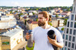 © sofiko14 - A man stands on a rooftop, holding a water bottle and yoga mat while looking out over the city skyline