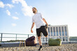 © sofiko14 - A man with a beard and long hair is stretching his quadriceps on a gravel rooftop with a modern building in the background