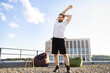 © sofiko14 - A man with a beard and long hair stretches his arms overhead on a rooftop with beanbag chairs and a building in the background