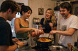 © Iryna - Four young adults cooking pasta and laughing together in a home kitchen, suitable for content about friendship, home cooking, and happy social gatherings.