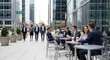 © Flowrender - Professionals on a coffee break at an outdoor cafe in a busy financial district, while other colleagues walk by, reflecting urban corporate life and networking.