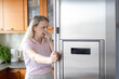 © Ina - Middle aged woman reacts to unpleasant smell after opening broken refrigerator in home kitchen. Household emergency, spoiled food, appliance failure, unexpected expense and modern home problem concept