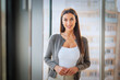 © gzorgz - Confident businesswoman standing in a sunlit office by the window