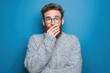 © Oleksandr - Portrait of a bearded man in a knit sweater with glasses whispering a secret against a blue background
