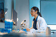 © Crystal - Female scientist wearing safety glasses and lab coat, focusing on computer screen while conducting research in a modern lab