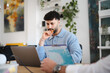 © Studio Marmellata - A man with curly hair sits at a desk, looking intently at a laptop screen while holding a pencil to his chin. He is in a modern office space with plants and artwork.