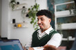 © Studio Marmellata - A young man smiles while working on a laptop in a modern office setting with plants.