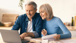 © Prostock-studio - A couple is sitting at a kitchen table looking at a laptop. They appear to be discussing financial matters while holding papers, looking engaged and focused on their task.