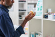 © pressmaster - Middle aged man examining supplement bottle in pharmacy aisle, comparing product information for purchase decision. Useful for healthcare retail, medication choice, consumer wellness