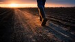 © Popelniushka - Low sun silhouette of a rubber-booted farm worker crossing dark soil furrows
