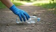 © Rafiuddin - Person wearing a blue glove picking up a discarded plastic bottle from a dirt path