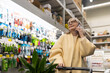 © Ivan Traimak - Mature woman smiling, engaging in a phone call, pushing a shopping cart in a garden center