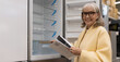 © Ivan Traimak - Smiling senior woman examining an empty refrigerator display in a retail store