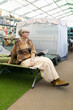 © Ivan Traimak - Mature woman wearing glasses and poncho, sitting on a cot in a camping supply store