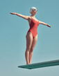 © peopleimages.com - Diving board, woman and stretching by blue sky for swimming, exercise or sport in swimwear by space. Female person, confident swimmer and balance with fitness of diver in gear outdoor in low angle