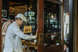 © Rakchanok - family small business coaching, senior cafe owner giving instruction to young son barista standing at storefront, learning by doing with new generation, leadership daily operation guidance concept.