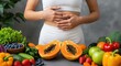 © Alice E - Woman in white fitness wear touches her stomach behind fresh fruits and vegetables including papaya, berries, lettuce, and tomatoes. Perfect for wellness and healthy eating content.