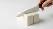 © Lee - A hand expertly slices a block of silken tofu into perfect cubes with a sharp kitchen knife