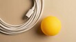 © tonstock - Minimalist flat lay composition of a white braided USB cable and yellow ball on a neutral beige background.