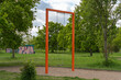 © Jakob - Orange swing set stands empty in grassy park. Trees surround area, sky bright with clouds. Quiet scene suggests calm, peaceful day. Ideal for advertising, travel, or childhood themes