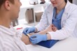 © New Africa - Doctor in protective gloves putting medical tourniquet on patient's arm at white desk indoors, closeup