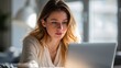 © The Little Hut - Young woman focused on laptop screen, working remotely or studying from home in soft natural light