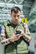 © StockMediaSeller - Young male traveler using smartphone while standing in modern airport departure area