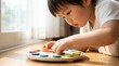 © Yauhen - A young Asian boy focuses on a colorful wooden clock toy on a wooden floor. Montessori learning in a bright, natural setting. Ideal for parenting blogs and educational materials.