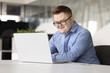 © fizkes - Smiling professional male office manager with Down syndrome working on laptop, review tasks to-do, engaged in administrative remote workflow seated at desk in contemporary workspace. Inclusivity, tech