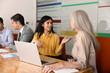 © fizkes - South Asian businesswoman engaging in conversation with woman colleague during group meeting in corporate office. Professional communication, business ideas exchange, collaborative decision making