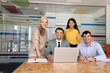 © fizkes - Multiethnic businesspeople smiling at camera gather at conference room with laptop, posing for professional corporate portrait. Office meeting, business teamwork, team collaboration, diversity concept