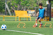 © chokniti - World cup concept with soccer ball or football player, youth soccer training boy athlete field drill agility hurdle soccer ball outdoor field sport practice blue vest green grass fence background
