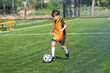 © chokniti - World cup concept with soccer ball or football player, young boy playing soccer on outdoor field, orange bib, active sport practice and focused dribble on green grass