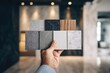 © Febri - Hand holding sample tiles of various textures and colors in a showroom