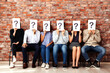 © Supto - Group of diverse people sitting in a row holding question mark signs over their faces expressionless