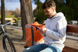 © Oscar - Delivery man checking smartphone messaging app on park bench