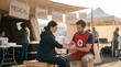 © Maksym - A disaster relief medic in a red tabard treats a minor wound for a woman seated on a crate outside a temporary shelter, a makeshift outdoor 3