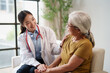 © Tj - Young Asian female doctor in white coat talking to elderly woman, holding hands and placing a comforting hand on her shoulder, providing empathetic home healthcare