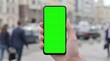 © SUPERPOS - Person holding green screen smartphone mockup in urban street