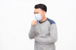 © Torao - Man wears mask, coughs into fist. He appears unwell, slightly distressed. Plain background highlights his symptoms clearly. Ideal for health, illness, or pandemic-related content